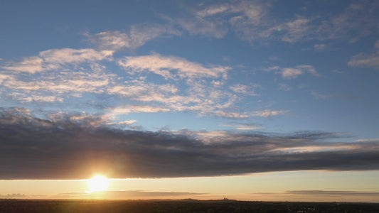 Video - Timelapse - Sun sets below storm clouds above urban landscape