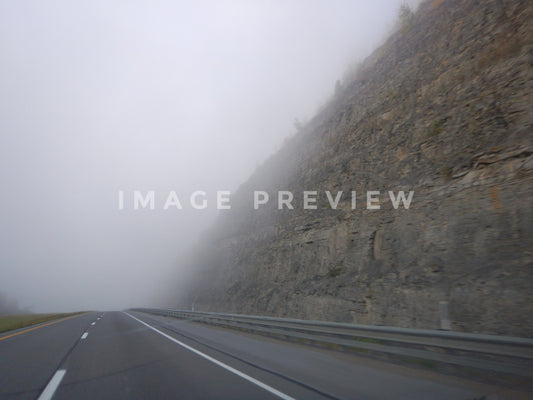 Photo - Driving by rocky cliffside in fog beside interstate highway